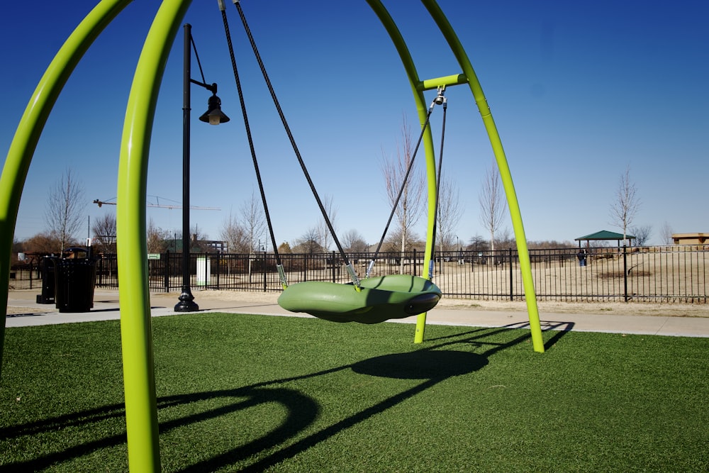a green swing set in a park with a blue sky in the background