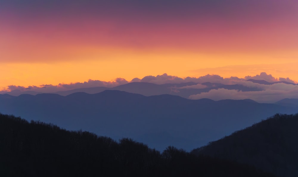 une vue au coucher du soleil sur une chaîne de montagnes avec des nuages dans le ciel