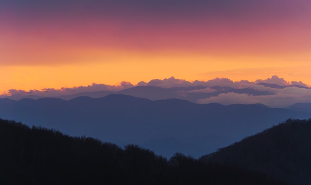 a sunset view of a mountain range with clouds in the sky