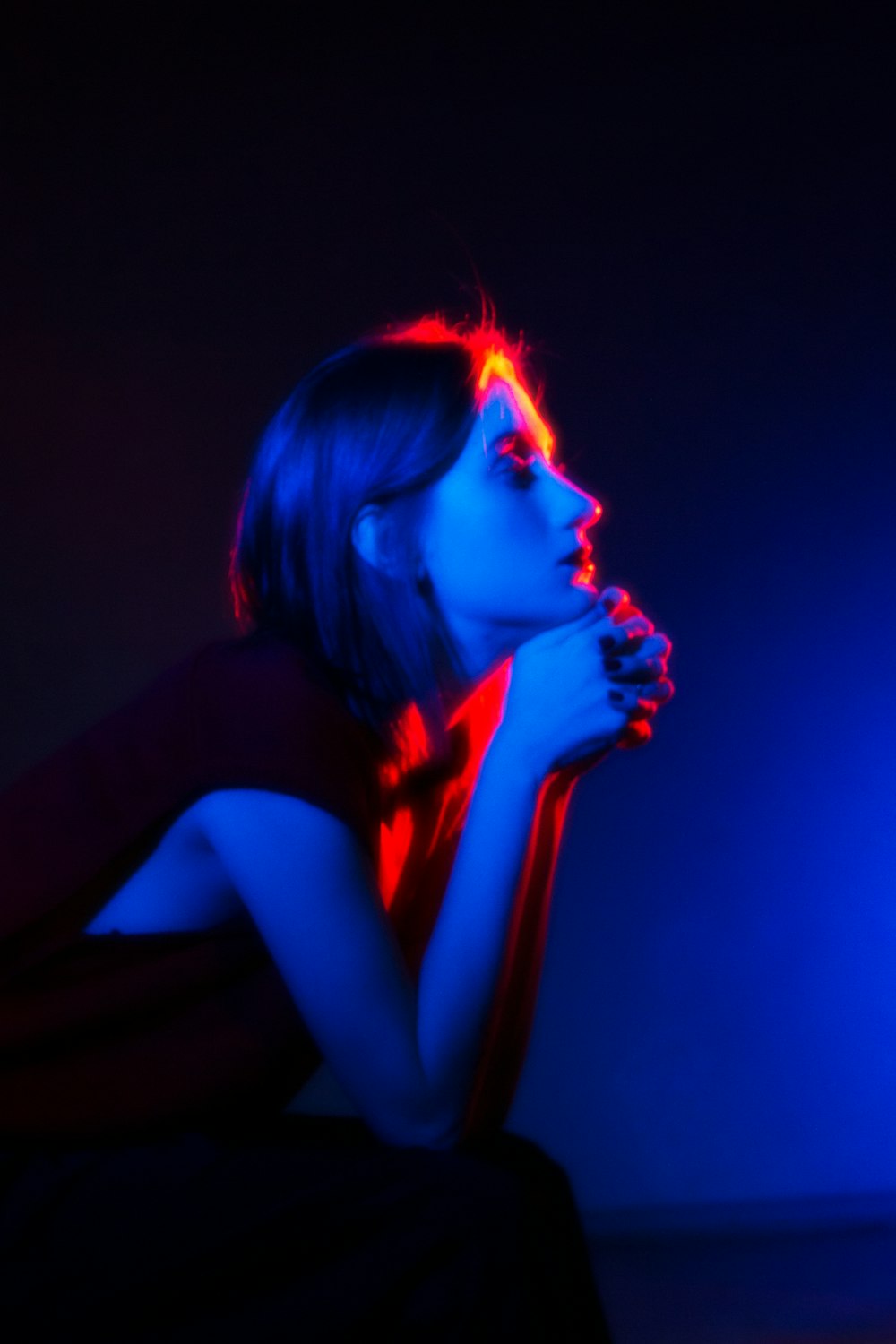 a woman sitting in a dark room with her hand on her chin