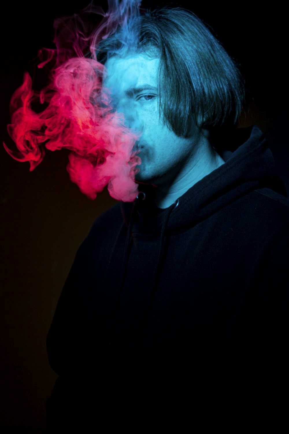 Un hombre fumando un cigarrillo con humo rojo y azul saliendo de su boca