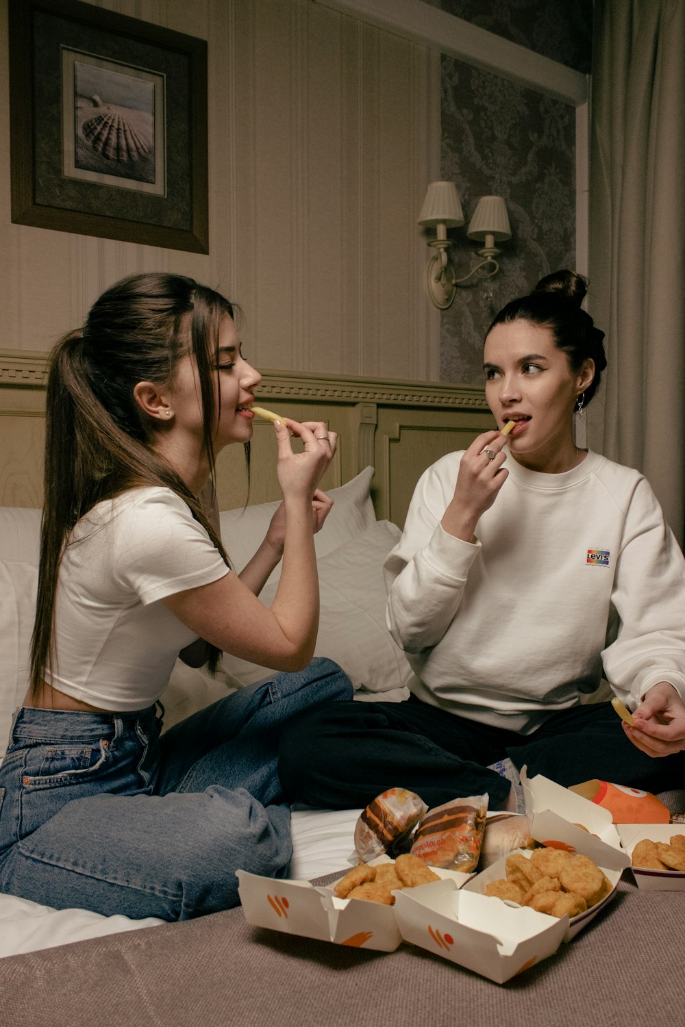 Due donne che si siedono su un letto che mangiano cibo