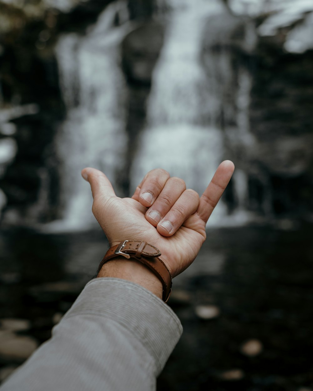 a person holding their hand out in front of a waterfall