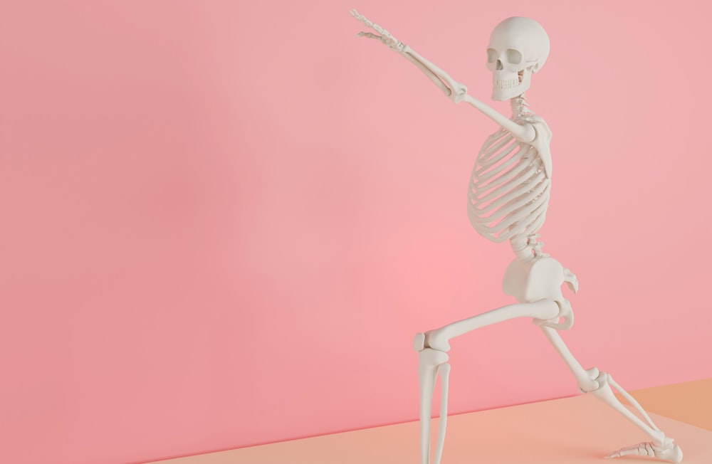 a skeleton holding a tennis racquet on a pink background