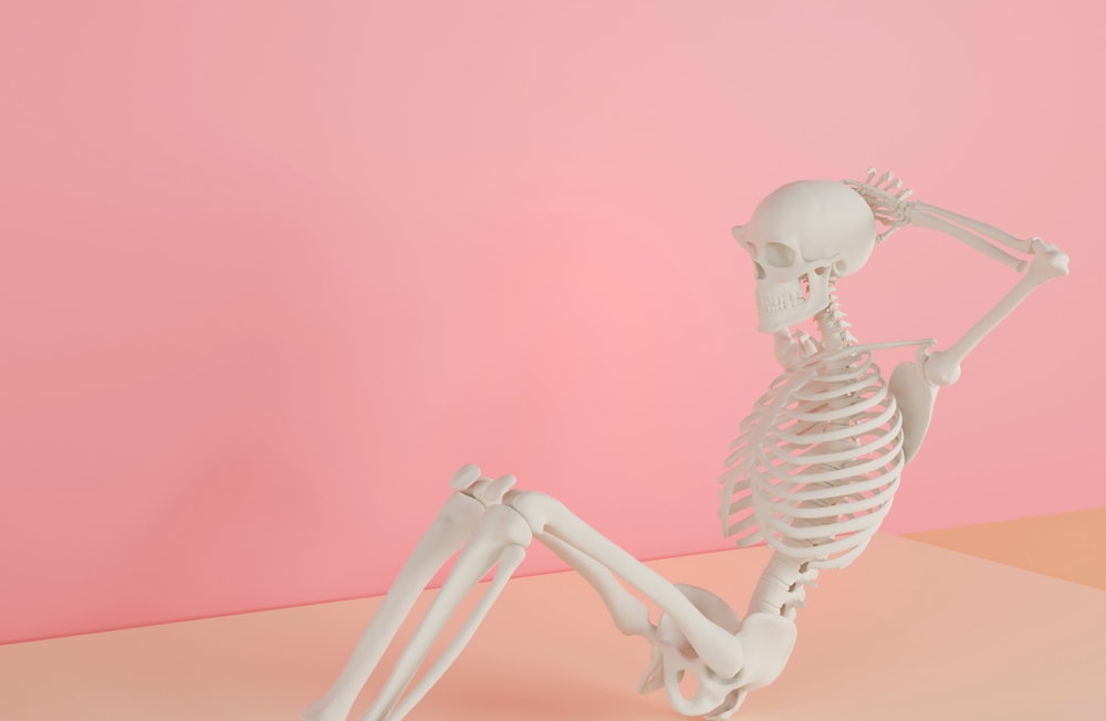 a skeleton sitting on its back on a pink surface