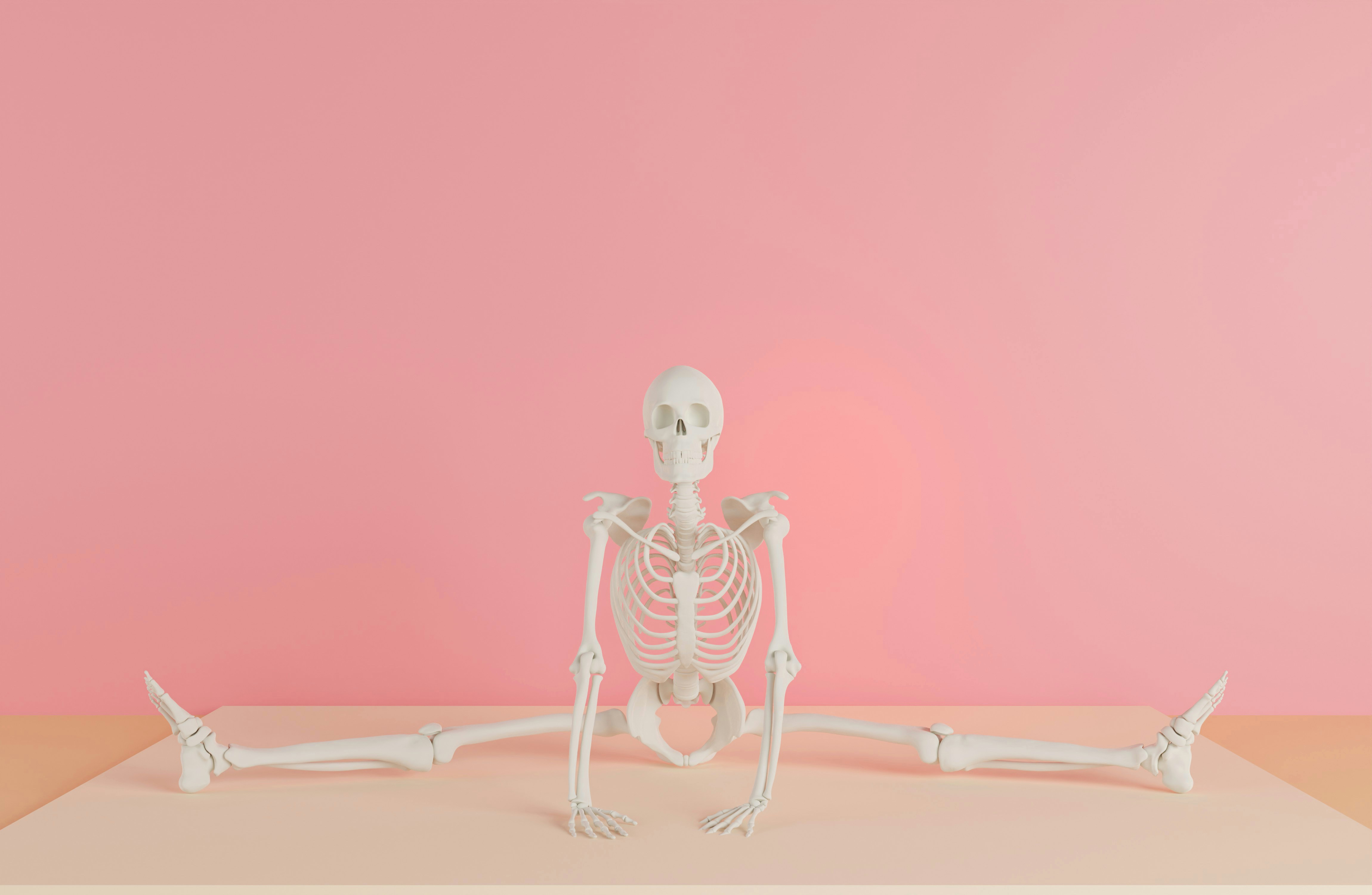 a skeleton sitting on a table in front of a pink wall