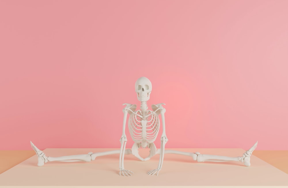 a skeleton sitting on a table in front of a pink wall