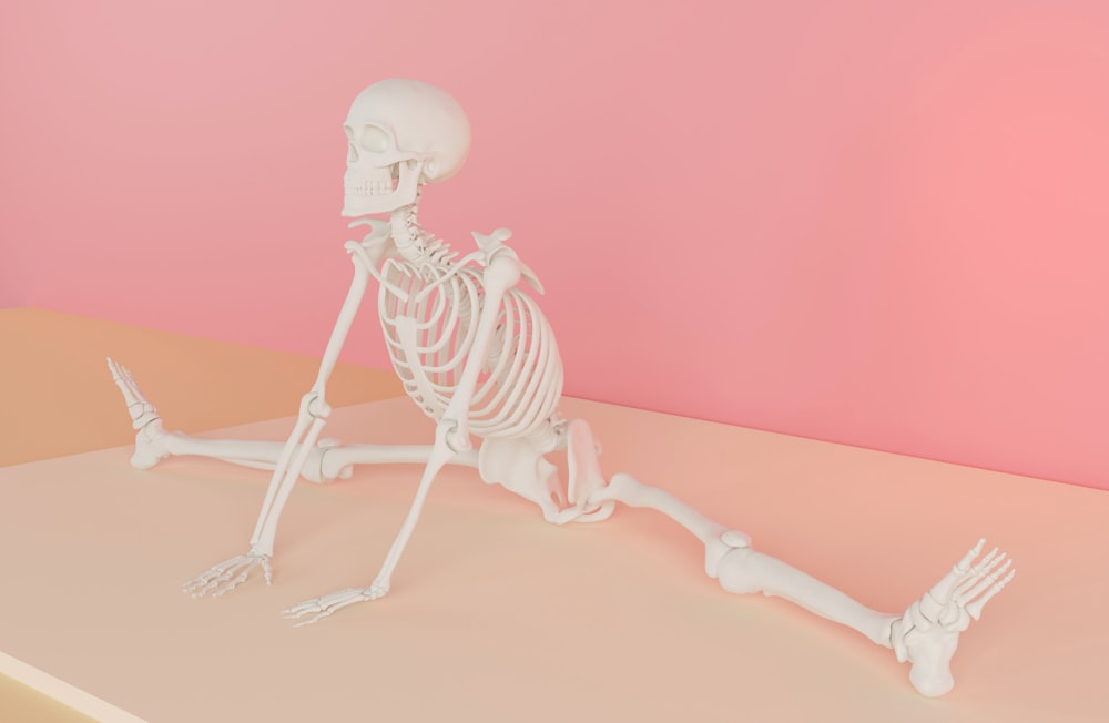 a skeleton sitting on top of a table next to a pink wall