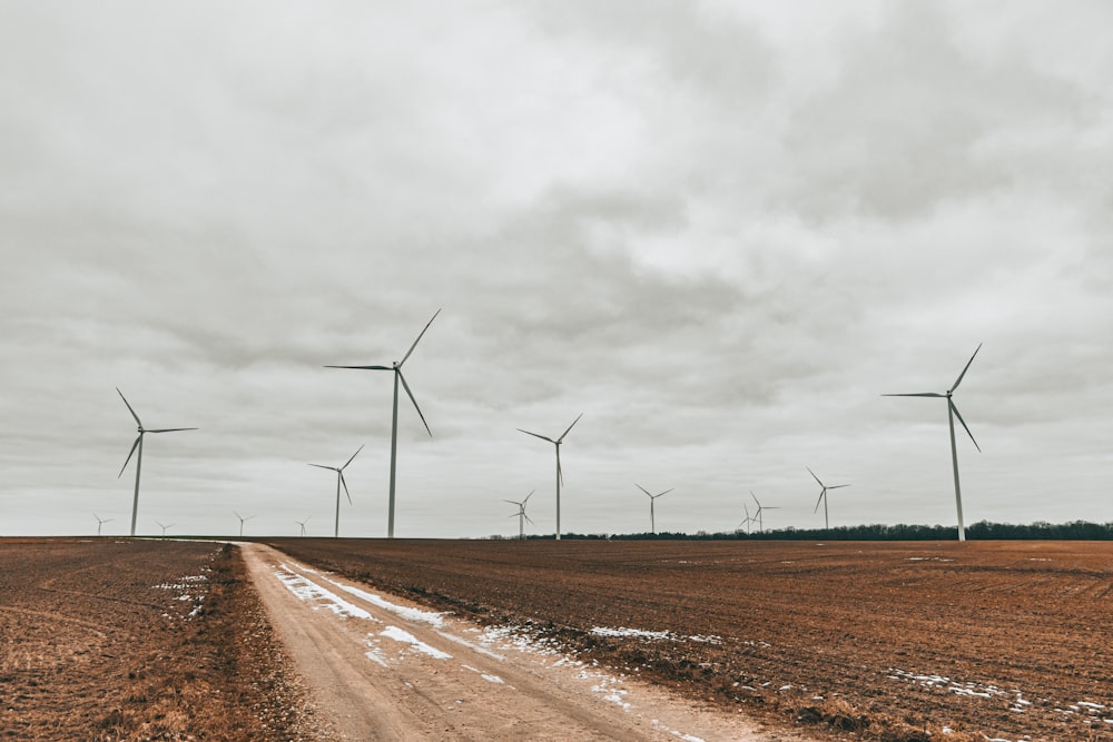 a dirt road in front of a row of wind turbines