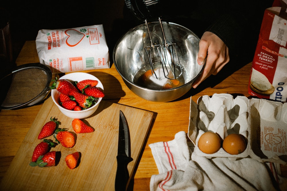 a wooden table topped with a bowl of strawberries and eggs