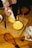 Hands are using a piping bag to add cream filling between two layers of cake on a wooden cutting board. Nearby, there is a serrated knife, an empty cake ring mold, a bowl with something red, an egg carton with eggs, and a whisk.