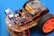 An assembled robot car featuring multiple electronic components, including a circuit board, batteries, sensors, and wires. The car framework is made of light-colored wood, and it has two large black wheels with orange hubs. The background is a solid blue color.