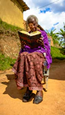 A senior woman relaxing with a book on a sunny hotel balcony.