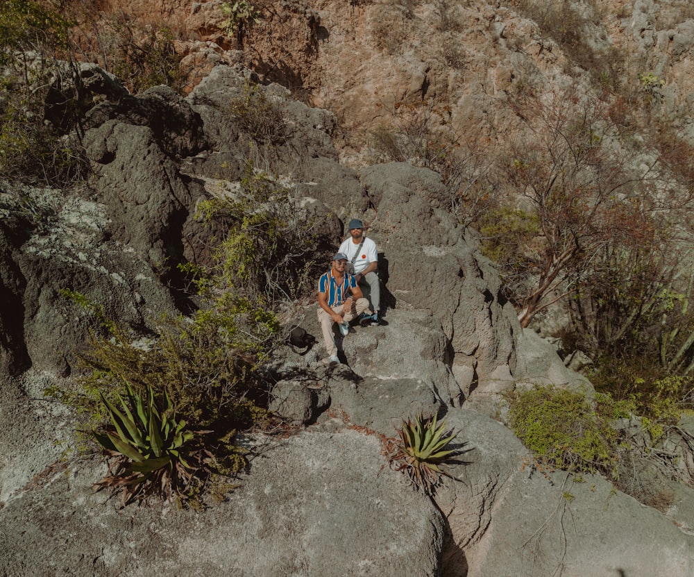 a couple of people sitting on top of a large rock