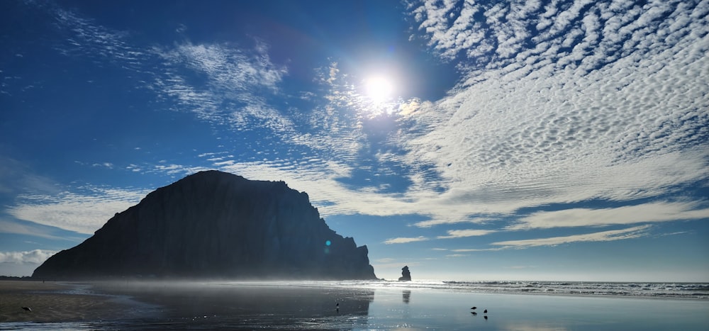 the sun shines brightly on a beach with a rock formation in the background