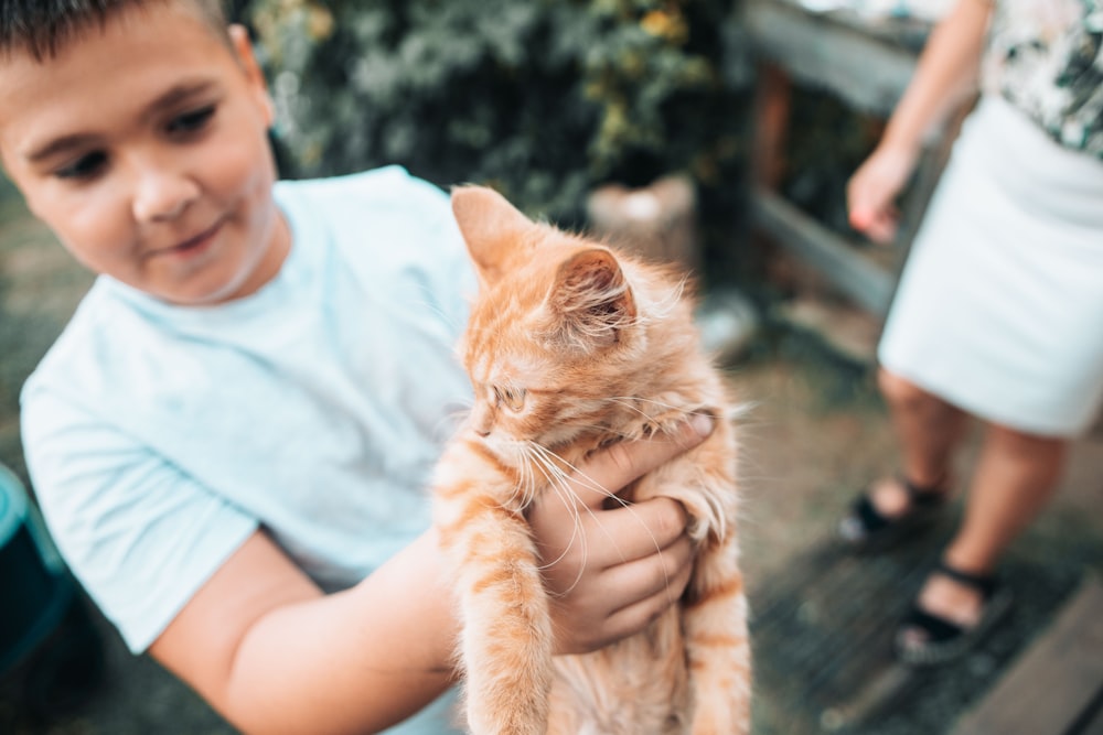 a young boy holding a small orange cat