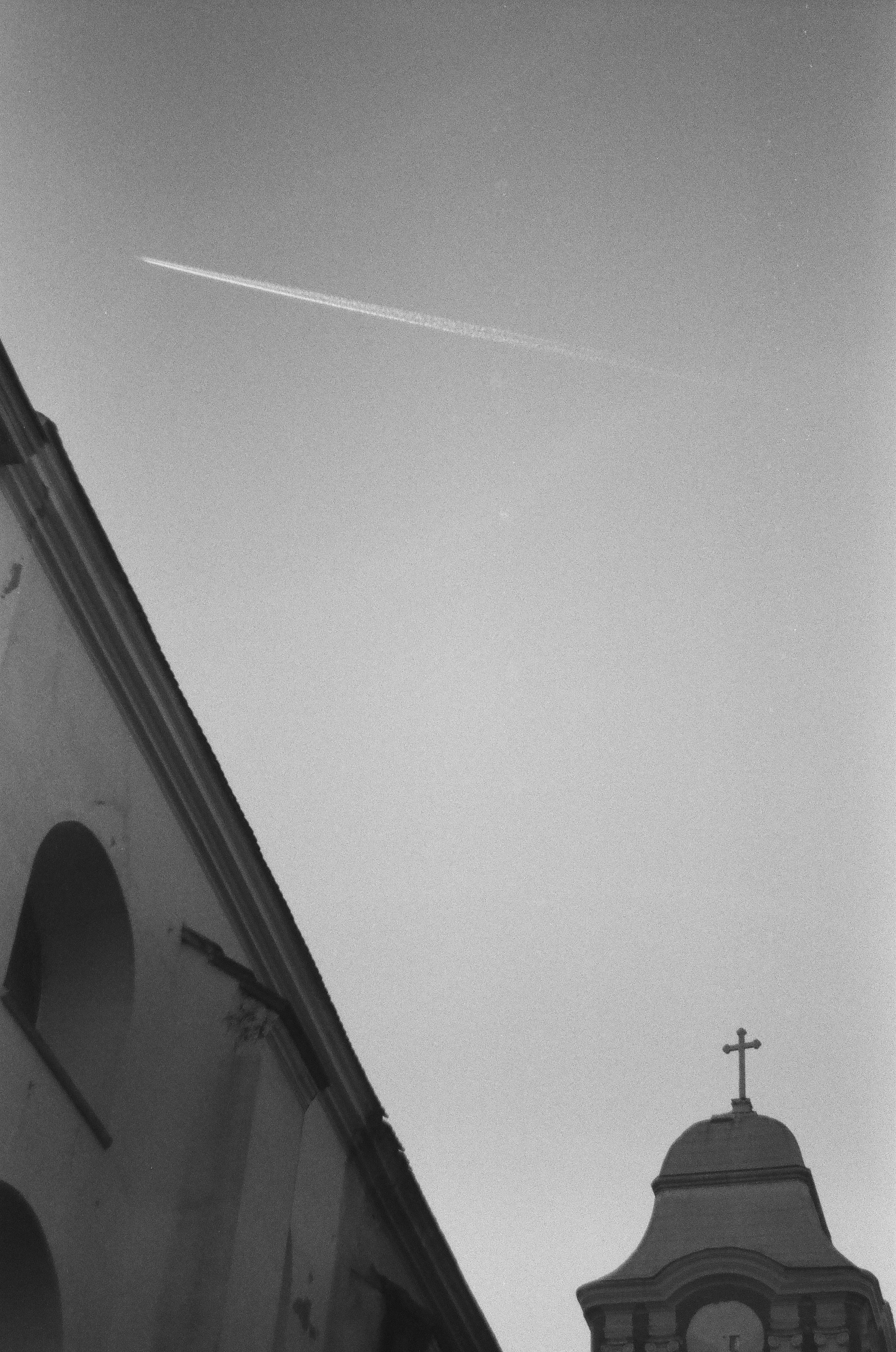 A black and white photo of a church steeple and a plane in the sky ...