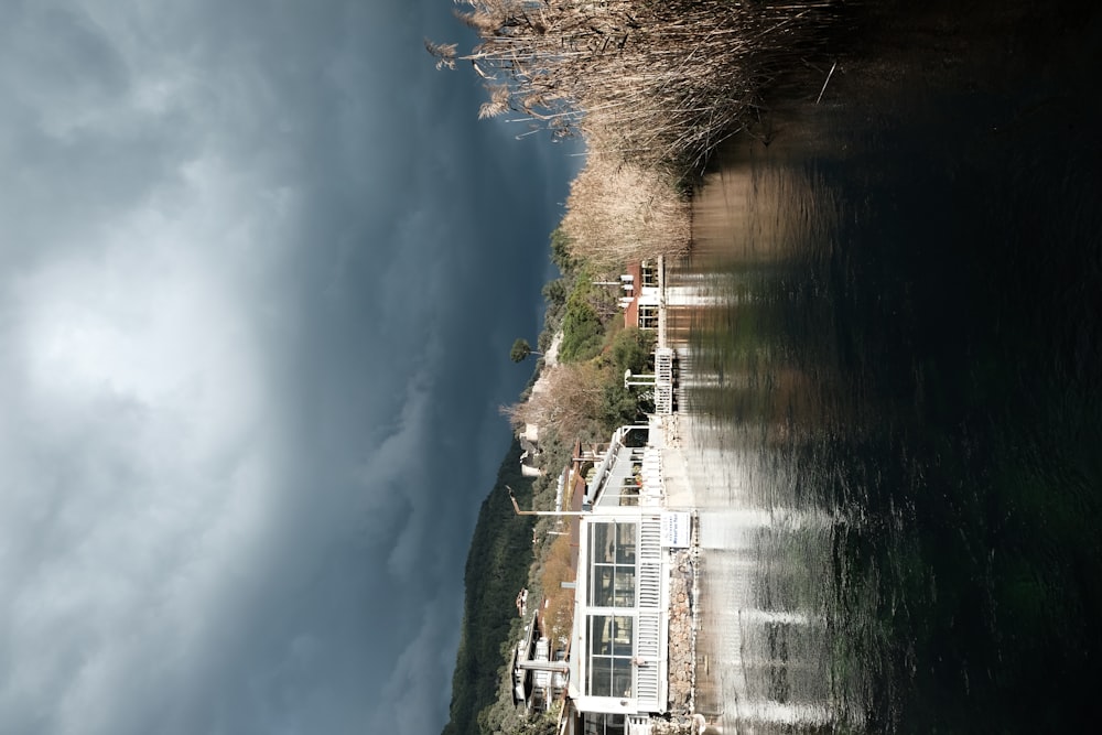 a house sitting on the side of a river under a cloudy sky