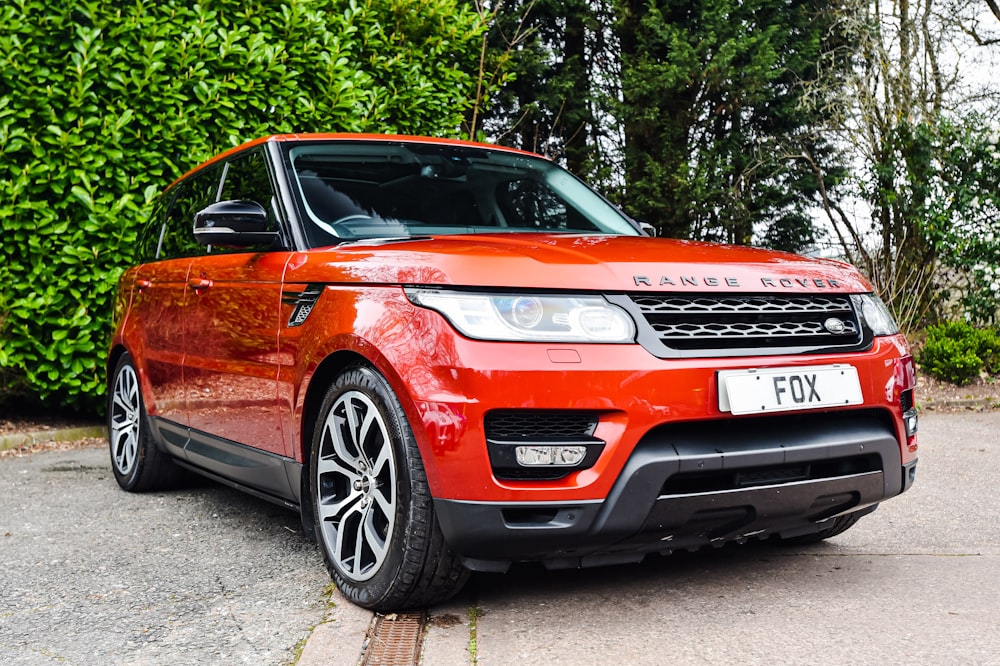 a red range rover parked in front of a bush