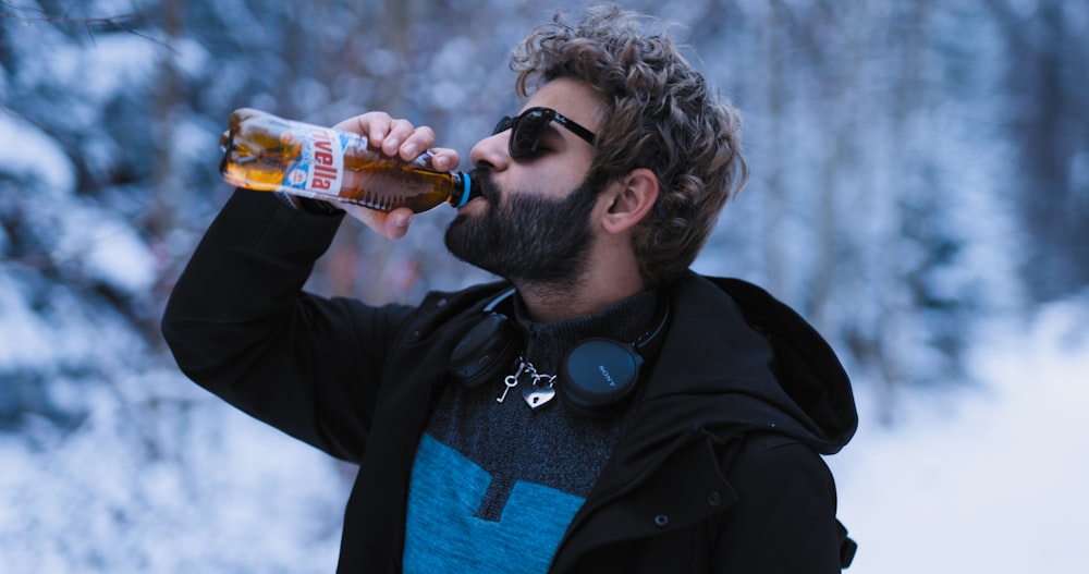 a bearded man drinking a beer in the snow