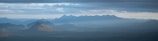 A wide-angle view of a misty mountain range under a soft morning sky.