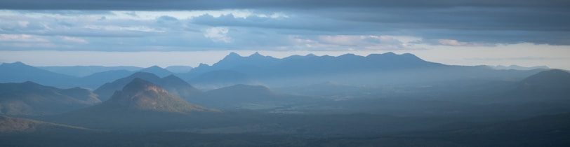 A wide-angle view of a misty mountain range under a soft morning sky.