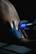 A person is receiving a tattoo on their back. The tattoo artist is wearing black gloves and is using a tattoo machine with a blue cover. The design is partially sketched on the person's skin.