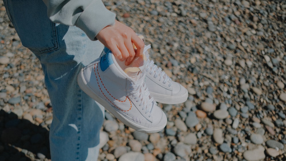 a person holding onto a pair of white sneakers