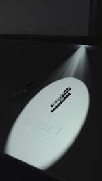 A beam of light illuminates a sleek, reflective surface with a pen positioned horizontally. The light creates a spotlight effect, highlighting the text '@ZOOM L11'. The surrounding area is dark, adding contrast to the illuminated section.