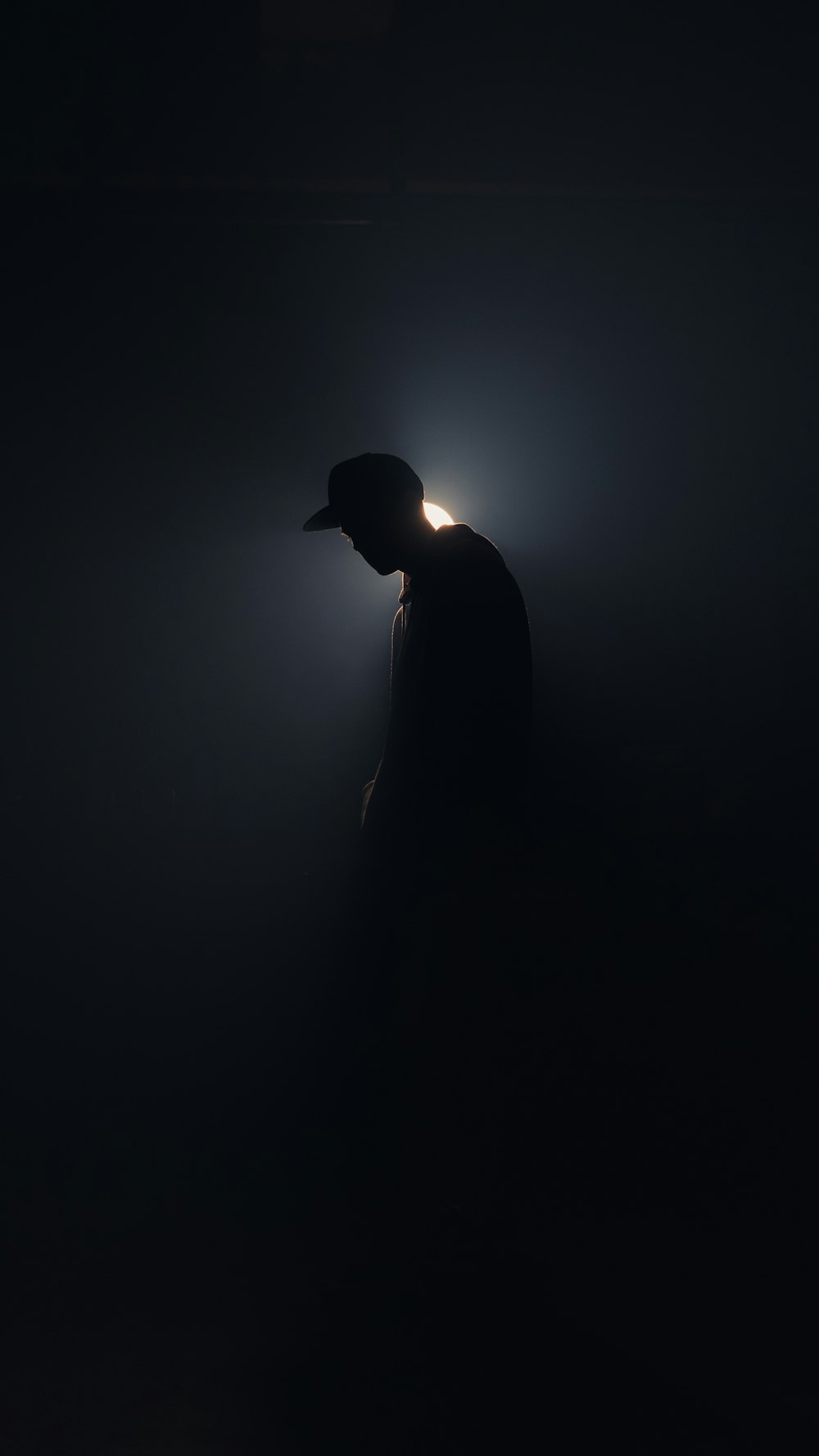 a person standing in the dark with a baseball cap on