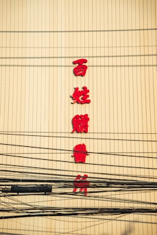 Red Chinese characters are displayed vertically on a yellow wall, with numerous black electrical cables crossing in front.