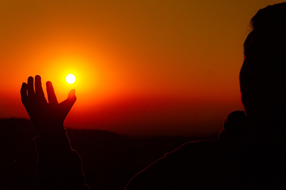 une personne levant la main vers le soleil