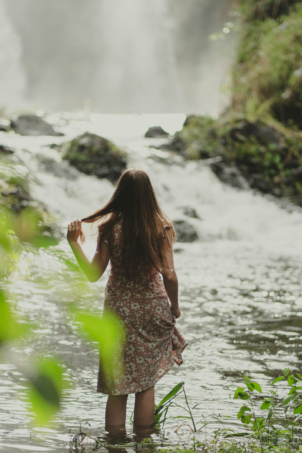 a woman standing in the water near a waterfall