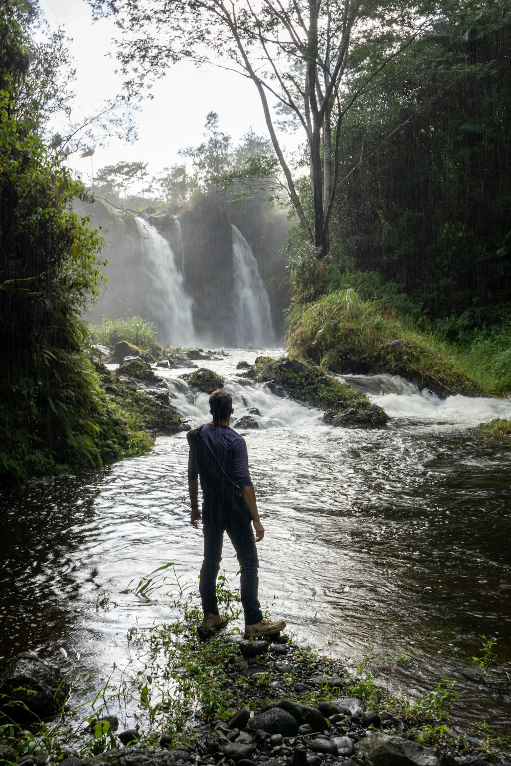 a man standing in the middle of a river next to a waterfall