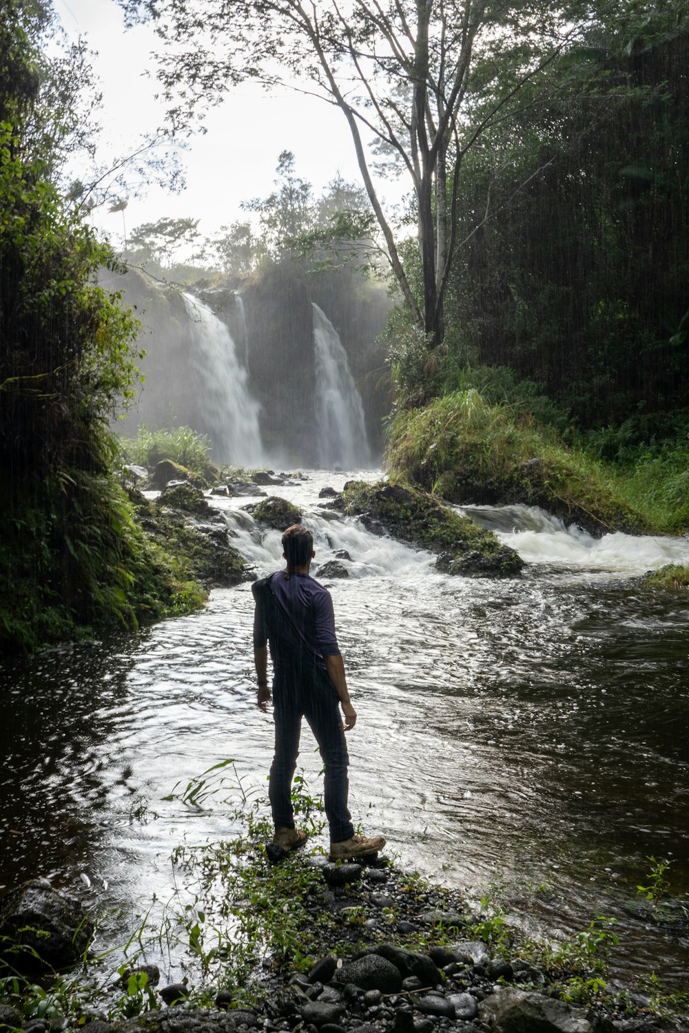 Un uomo in piedi nel mezzo di un fiume vicino a una cascata