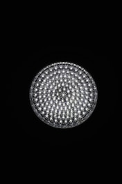 A circular light source composed of multiple small, bright LED bulbs, arranged densely in a grid pattern against a black background. The LEDs emit a cool white glow, creating a striking contrast.