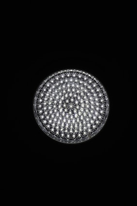 A circular light source composed of multiple small, bright LED bulbs, arranged densely in a grid pattern against a black background. The LEDs emit a cool white glow, creating a striking contrast.