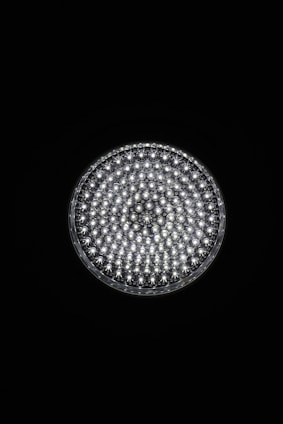 A circular light source composed of multiple small, bright LED bulbs, arranged densely in a grid pattern against a black background. The LEDs emit a cool white glow, creating a striking contrast.