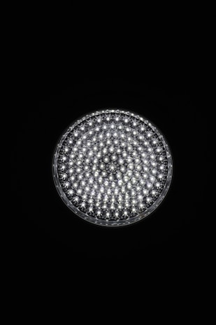A circular light source composed of multiple small, bright LED bulbs, arranged densely in a grid pattern against a black background. The LEDs emit a cool white glow, creating a striking contrast.