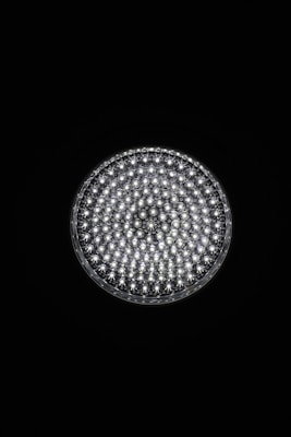 A circular light source composed of multiple small, bright LED bulbs, arranged densely in a grid pattern against a black background. The LEDs emit a cool white glow, creating a striking contrast.