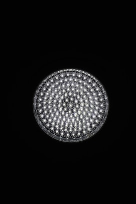 A circular light source composed of multiple small, bright LED bulbs, arranged densely in a grid pattern against a black background. The LEDs emit a cool white glow, creating a striking contrast.