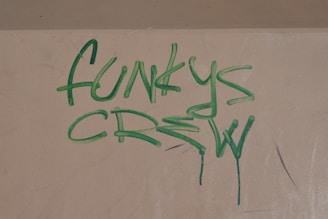 Graffiti text reading 'Funkys Crew' is painted in green on a beige wall, with some drips visible at the bottom of the letters.