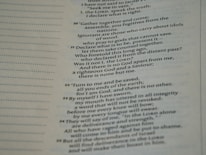 A close-up view of a page from a Bible, featuring passages in both regular and bold text. The text is formatted in a column with numbers preceding certain lines, set against a background of light-colored paper.
