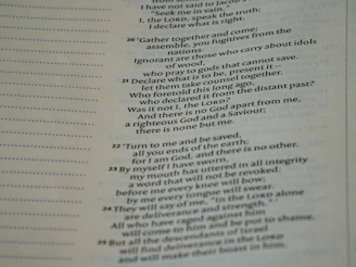 A close-up view of a page from a Bible, featuring passages in both regular and bold text. The text is formatted in a column with numbers preceding certain lines, set against a background of light-colored paper.