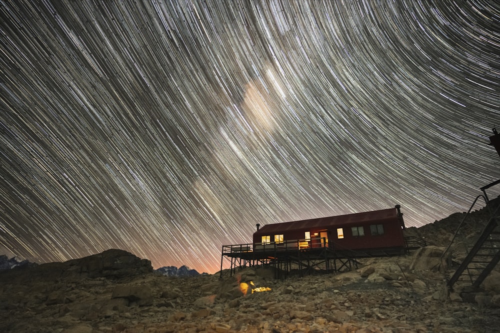 a red house sitting on top of a hill under a star filled sky