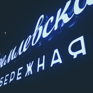Brightly-lit Cyrillic letters on a dark background, possibly a neon sign, spelling out words in Russian.