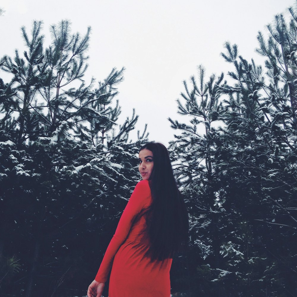a woman in a red dress standing in front of trees