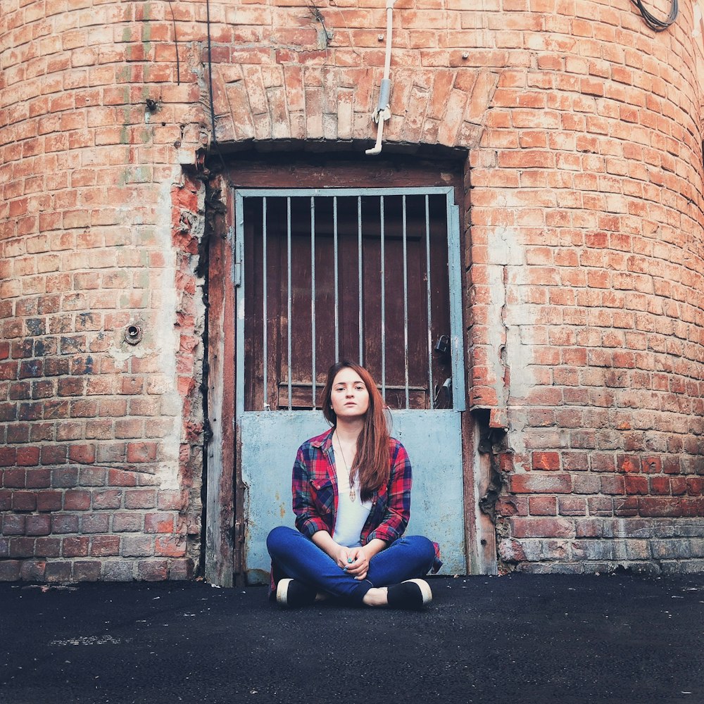 a woman sitting on the ground in front of a brick building