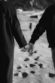 Couple walking hand in hand along the sandy beach with footprints behind them.