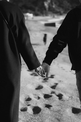 Couple walking hand in hand along the sandy beach with footprints behind them.